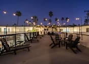 Thumbnail 56 of 64 - A patio with chairs and a table is lit by string lights at Ocean Breeze Terrace Apartment, Huntington Beach, CA