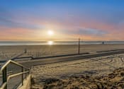 Thumbnail 45 of 64 - A sunset view of a beach with a metal railing in the foreground at Ocean Breeze Terrace Apartment, Huntington Beach
