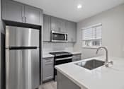 Thumbnail 1 of 14 - an empty kitchen with stainless steel appliances and white countertops at Charle Square Apartments, Costa Mesa
