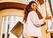 Thumbnail 7 of 10 - A woman with a white jacket and red pants is holding shopping bags.