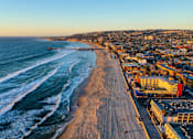 Thumbnail 2 of 10 - A beach with waves coming in and buildings in the background.