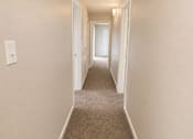 Thumbnail 24 of 38 - A long hallway with carpeted floors and white walls.