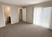 Thumbnail 27 of 38 - A room with a carpeted floor, a window with blinds, and a door leading to another room.