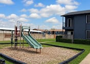Thumbnail 35 of 38 - A playground with a green slide and a blue building in the background.