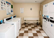 Thumbnail 37 of 38 - A laundromat with washers and dryers and a bench.