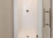 Thumbnail 30 of 52 - A white tiled shower with a drain in the middle.