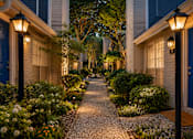 Thumbnail 39 of 52 - A cobblestone pathway leads between two houses with lit up lamps on either side.