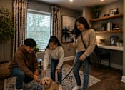Thumbnail 2 of 52 - A family of three is playing with a small dog in a living room.