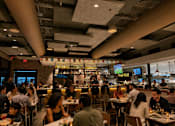 Thumbnail 49 of 52 - A restaurant with people dining and a bar in the background.