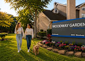 Thumbnail 9 of 52 - Two women walking a dog in front of a sign for Woodway Garden Townhomes.