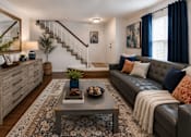Thumbnail 19 of 52 - A living room with a grey couch, a coffee table, and a staircase.