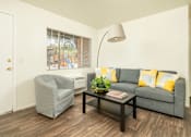 Thumbnail 13 of 13 - A grey couch with yellow pillows sits in a living room with a grey armchair and a coffee table.