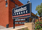 Thumbnail 10 of 17 - A sign for Columbus Terrace Apartments with a building in the background and balloons on top.