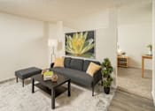 Thumbnail 19 of 20 - A grey sofa with a yellow pillow is in the middle of a room with a large painting of a yellow flower on the wall.