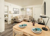 Thumbnail 9 of 13 - A dining table set with plates and glasses is in the foreground of a well-lit room with a couch and a bed in the background.