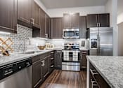 Thumbnail 1 of 35 - Modern kitchen with stainless steel appliances, tile backsplash, large island, granite countertops, and dark wood cabinetry.