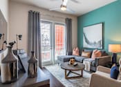 Thumbnail 7 of 35 - Modern apartment living room with sectional sofa, coffee table, accent wall, and patio access door.