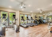 Thumbnail 20 of 26 - A spacious gym with a variety of equipment including treadmills, elliptical machines, and a fan.