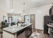 Thumbnail 1 of 26 - A kitchen with a granite countertop and a black refrigerator.