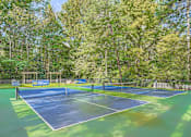 Thumbnail 28 of 39 - A tennis court surrounded by trees and a fence.