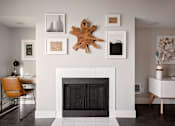 Thumbnail 6 of 26 - A fireplace with a leaf decoration above it and pictures on the wall.