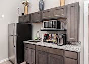 Thumbnail 22 of 28 - A kitchen with a black refrigerator and a black microwave on a granite countertop.