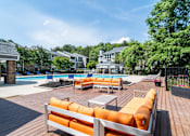 Thumbnail 34 of 37 - A wooden deck with orange cushions and a pool in the background.