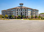 Thumbnail 13 of 26 - A large apartment building with a parking lot in front.