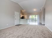 Thumbnail 30 of 38 - A spacious living room with a carpeted floor and a sliding glass door leading to a balcony.
