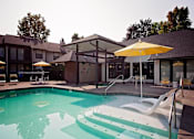 Thumbnail 2 of 24 - A pool with a yellow umbrella and white chairs.