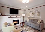 Thumbnail 20 of 24 - A living room with a fireplace, a couch, a chair, and a television.