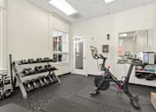 Thumbnail 21 of 32 - A gym room with a stationary bike, dumbbells, and other exercise equipment.