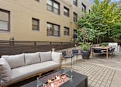 Thumbnail 22 of 32 - A patio with a couch, chairs, and a fire pit.