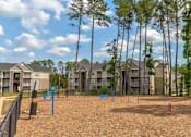 Thumbnail 29 of 31 - A playground with a sandy area and a fence in front of apartment buildings.