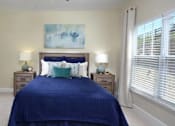 Thumbnail 6 of 31 - A bedroom with a blue bedspread and a painting on the wall.