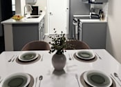 Thumbnail 15 of 40 - A dining table set with plates and cutlery is in the foreground of a modern kitchen.