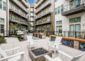 Thumbnail 35 of 35 - A patio area with white chairs and tables in front of apartment buildings.