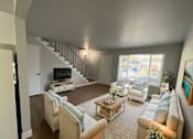 Thumbnail 1 of 21 - A living room with a staircase and a television.