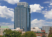 Thumbnail 76 of 78 - A tall building with a grey top stands in front of a sky with clouds.