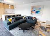 Thumbnail 32 of 40 - a living room with a black couch and a table and chairs at Brookland Apartments, Portland, OR