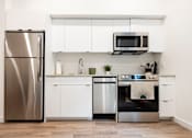 Thumbnail 23 of 40 - a white kitchen with stainless steel appliances and a stainless steel refrigerator at Brookland Apartments, Oregon