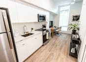 Thumbnail 9 of 40 - A modern kitchen with a refrigerator on the left and a dining area with a chair and a table at Brookland Apartments, Oregon