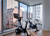 Thumbnail 2 of 78 - Two exercise bikes are placed in front of a window with a view of the city.