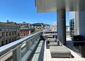 Thumbnail 17 of 78 - A balcony with grey cushioned seating and a metal railing overlooks a cityscape.