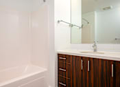 Thumbnail 55 of 78 - A white bathroom with a wooden cabinet and a white tub.