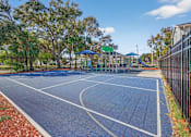 Thumbnail 14 of 19 - A basketball court is surrounded by a fence and trees.