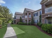 Thumbnail 11 of 31 - a walkway in front of an apartment building with green grass at Carrington Place at Wildewood, Columbia  