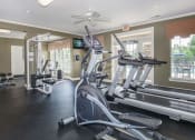 Thumbnail 13 of 31 - a gym with a row of workout equipment and windows at Carrington Place at Wildewood, Columbia, SC  