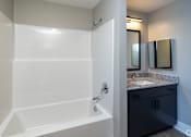 Thumbnail 13 of 23 - A white bathtub in a bathroom with a sink and mirror at Dunean Creek Apartments, Greenville