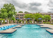 Thumbnail 1 of 17 - a swimming pool with chaise lounge chairs and umbrellas in front of an apartment building at The Bristol Apartments, Greenville, SC